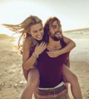 homem carregando mulher em suas costas com uma praia ao fundo