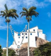 dois coqueiros com uma casa branca no topo de uma colina ao fundo