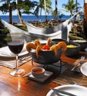 uma porção de camarão ao lado de uma taça de vinho e uma praia ao fundo